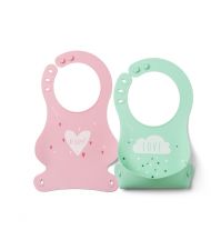 A pink silicone bib with heart design logo is placed next to a green silicone bib with a cloud design
